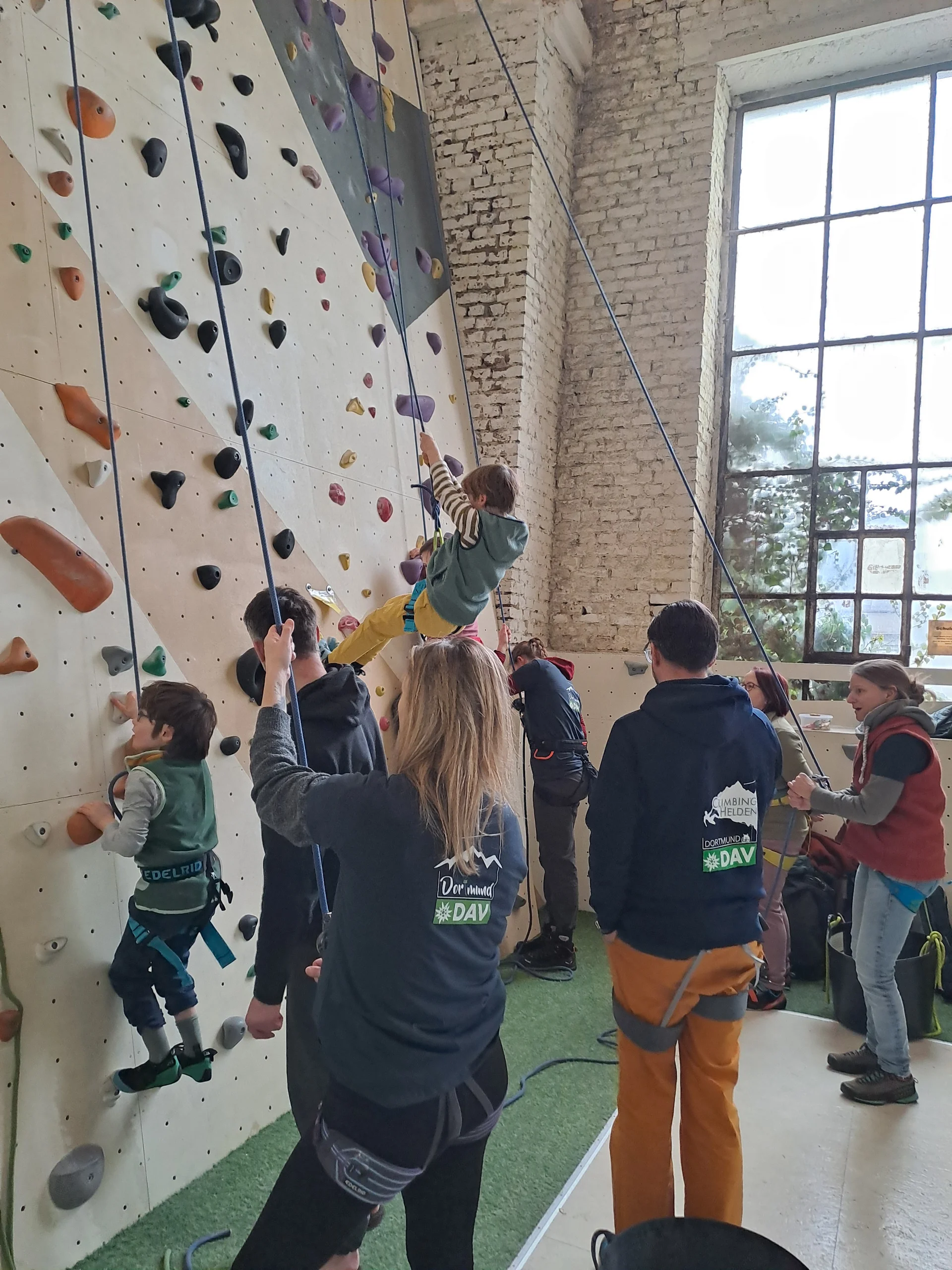 Kinder werden beim Seilklettern an einer Indoor-Kletterwand von Erwachsenen gesichert. | © DAV Dortmund