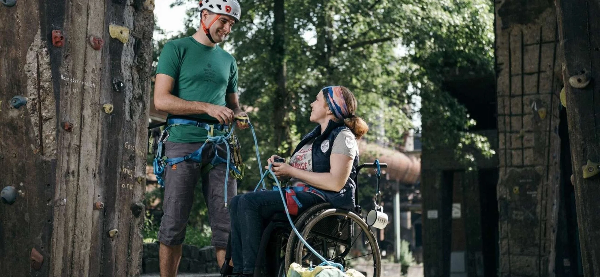 Kletterpartnerin im Rollstuhl unterhält sich mit einem stehenden Kletterer, beide tragen Gurtzeug. | © DAV Dortmund