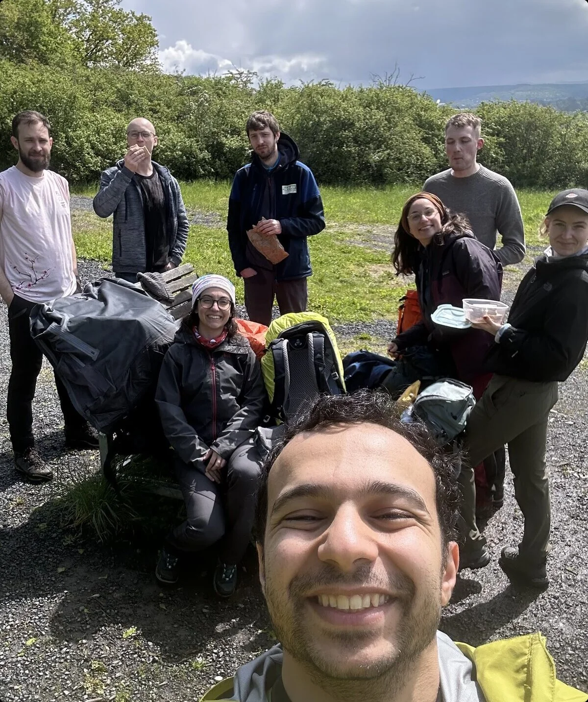 Ein junger Mann macht ein Selfie, im Hintergrund sieben weitere Personen mit Rucksäcken. | © u27 - JDAV