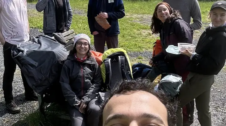 Ein junger Mann macht ein Selfie, im Hintergrund sieben weitere Personen mit Rucksäcken. | © u27 - JDAV