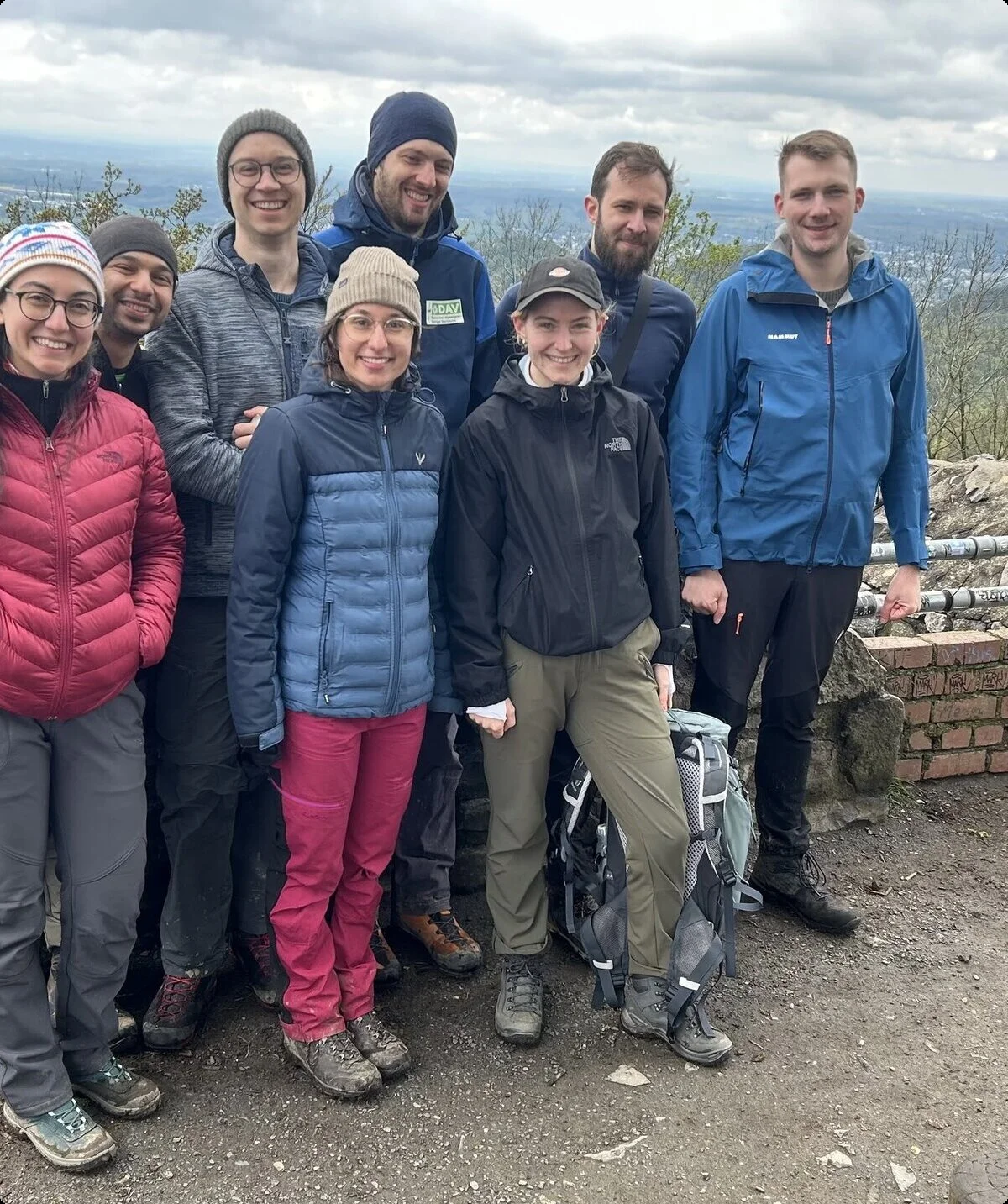 Acht Wandernde posieren vor einer Steinmauer mit weiter Aussicht ins Tal. | © u27 - JDAV