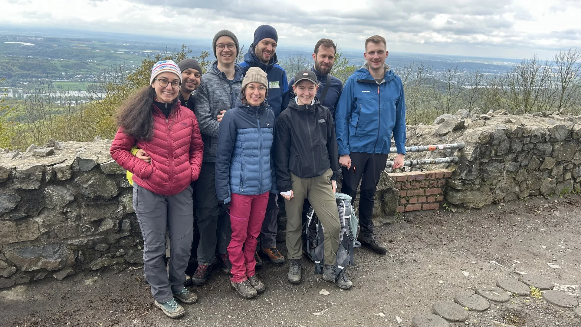 Acht Wandernde posieren vor einer Steinmauer mit weiter Aussicht ins Tal. | © u27 - JDAV