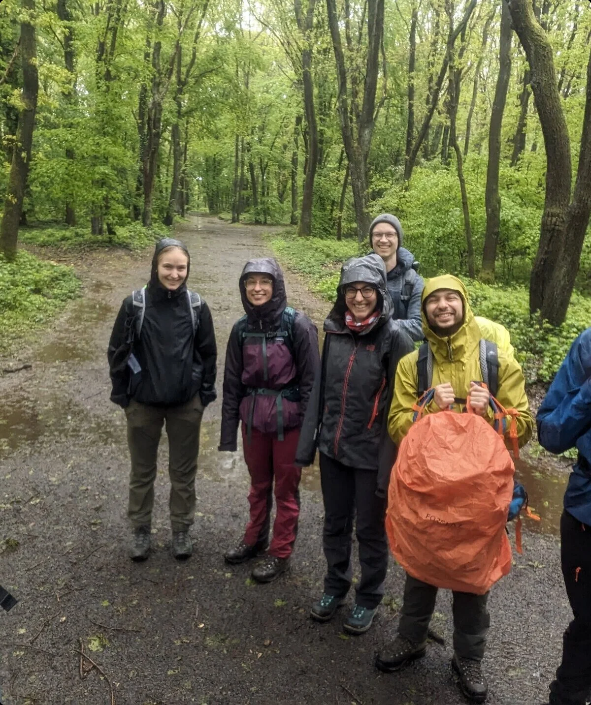 Acht Personen stehen mit Regenjacken auf einem Waldweg und lächeln in die Kamera. | © u27 - JDAV