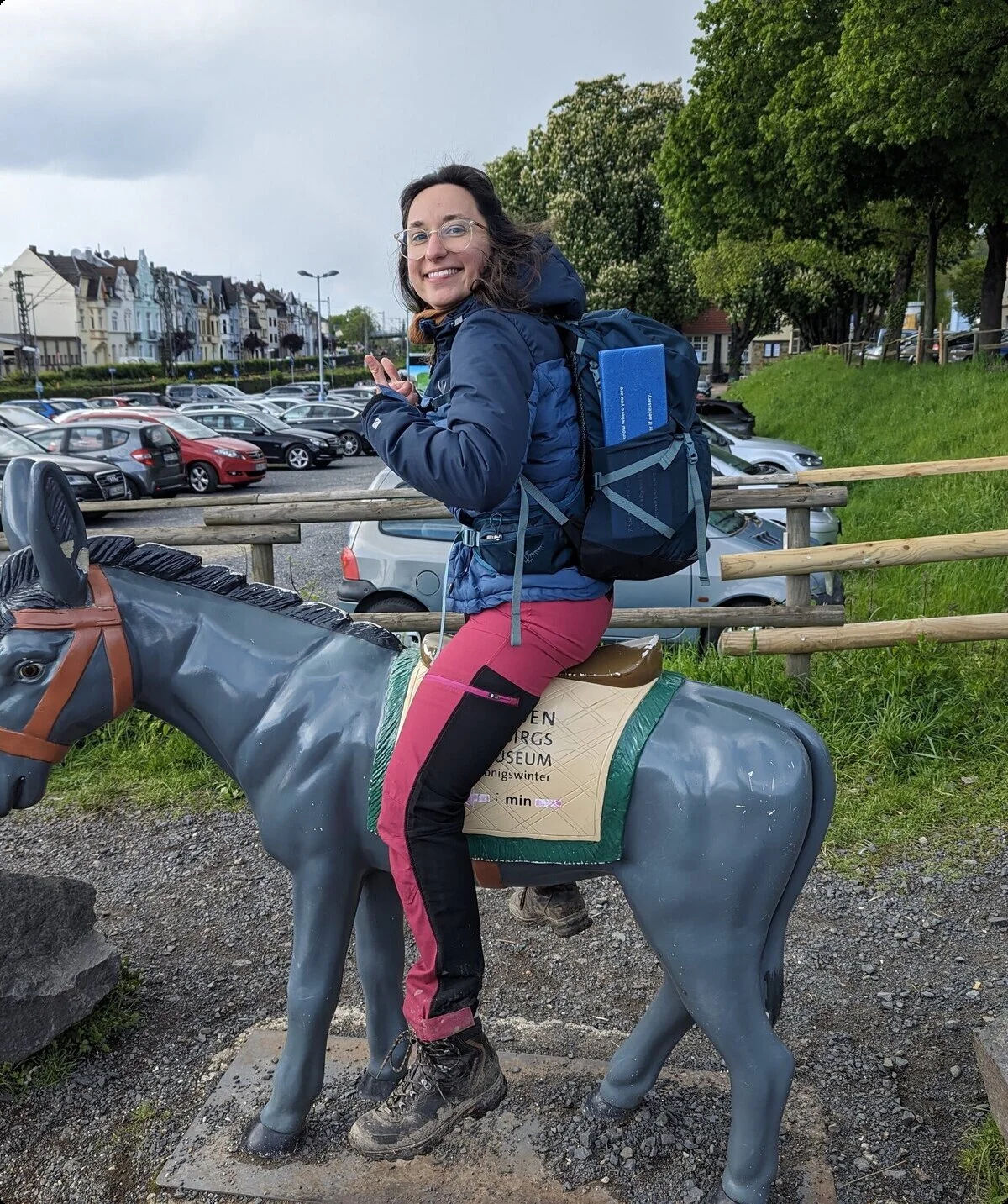 Eine Frau sitzt lachend auf einer Esel-Figur auf einem Parkplatz. | © u27 - JDAV