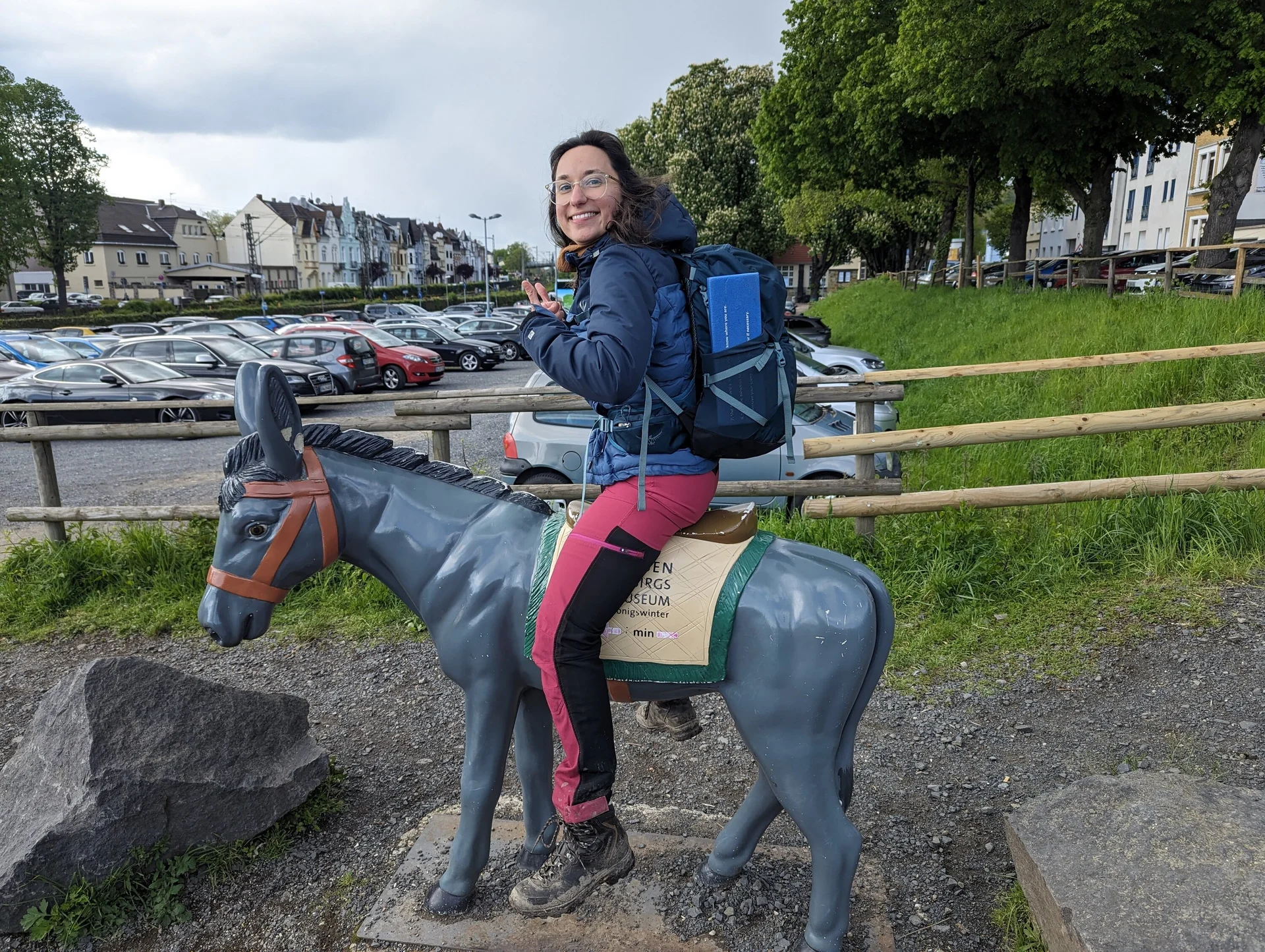 Eine Frau sitzt lachend auf einer Esel-Figur auf einem Parkplatz. | © u27 - JDAV