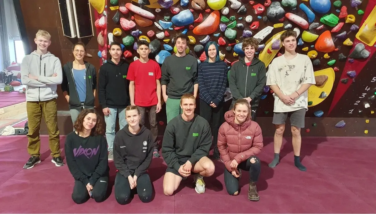 Jugendliche und junge Erwachsene stehen und knien vor einer bunten Boulderwand auf roter Matte. | © DAV Dortmund