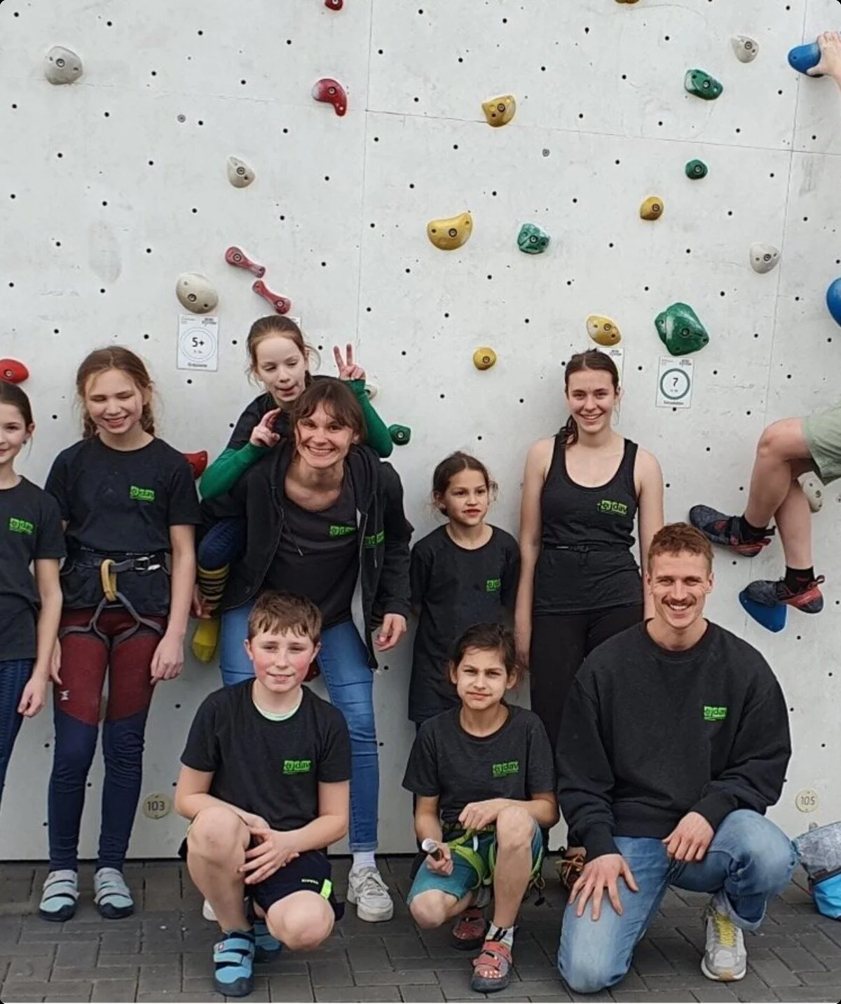 Kinder und Jugendliche in DAV-Shirts stehen vor einer Außen-Kletterwand mit bunten Griffen. | © DAV Dortmund