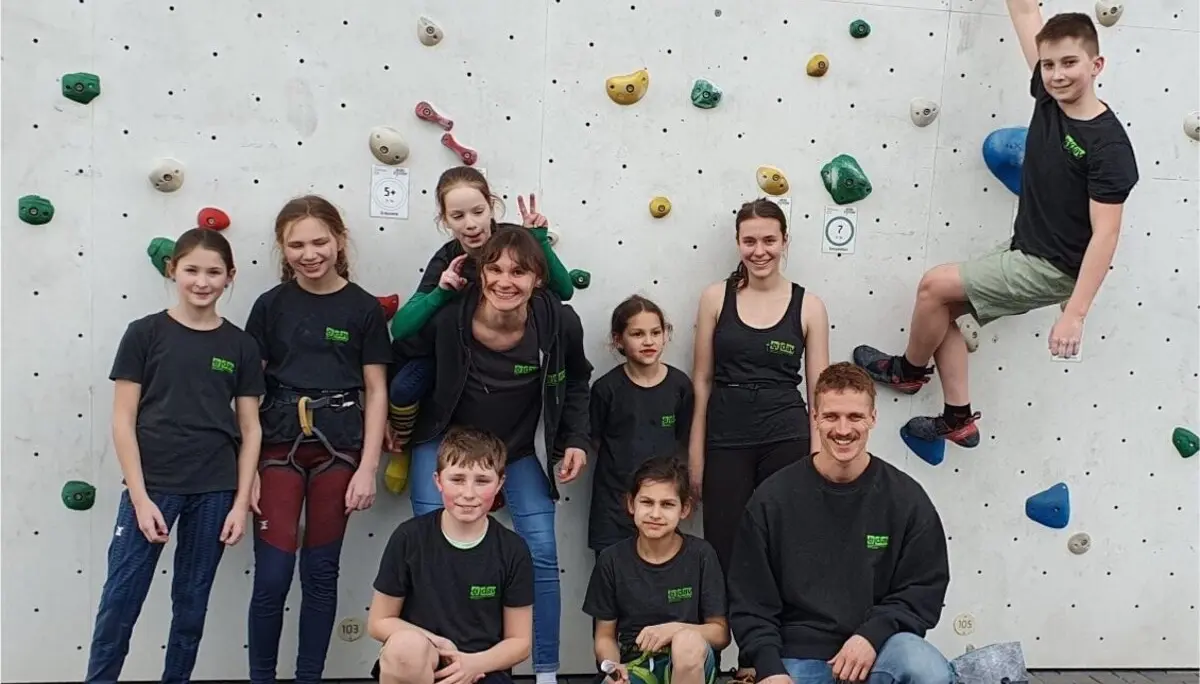 Kinder und Jugendliche in DAV-Shirts stehen vor einer Außen-Kletterwand mit bunten Griffen. | © DAV Dortmund