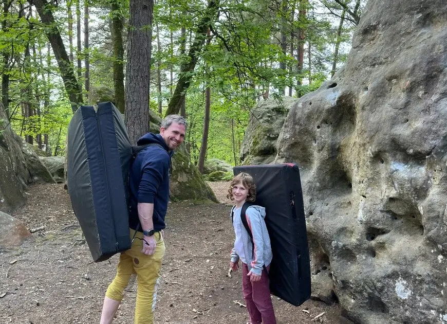 Ein Erwachsener und ein Kind mit Crashpads auf dem Rücken beim Bouldern im Wald. | © DAV Dortmund