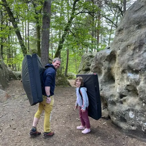 Ein Erwachsener und ein Kind mit Crashpads auf dem Rücken beim Bouldern im Wald. | © DAV Dortmund
